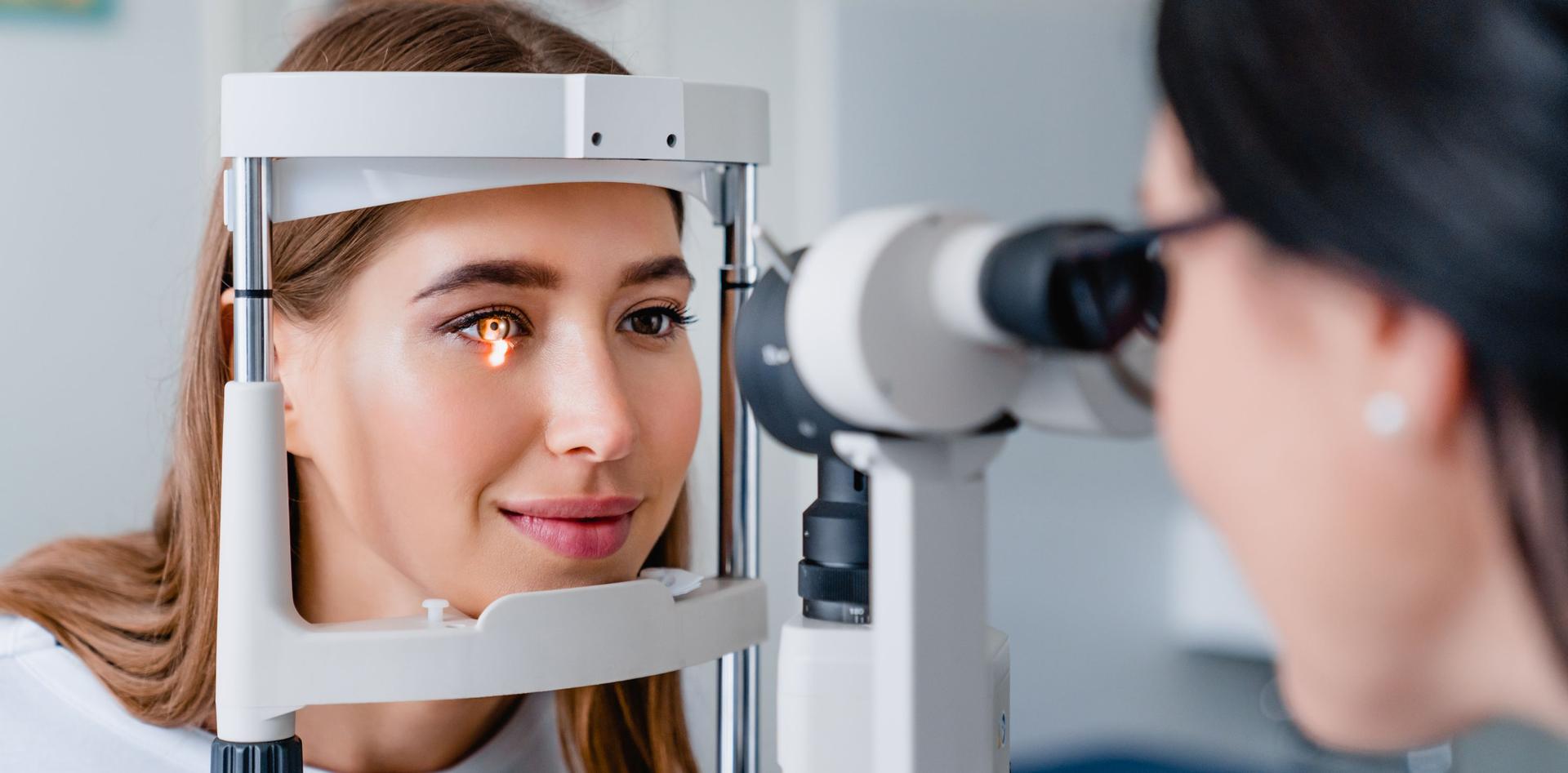 Das Bild zeigt eine Patientin, die bei einer Augenuntersuchung an einer Spaltlampe sitzt, während eine Augenoptikerin oder Augenärztin ihre Augen mit einem speziellen Untersuchungsgerät sorgfältig kontrolliert.