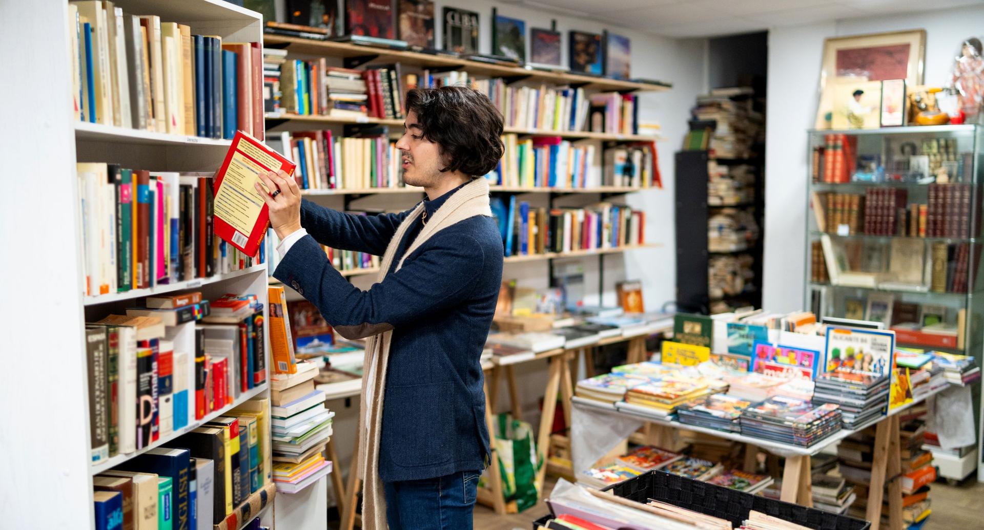Ein junger Mann sortiert in einer Buchhandlung Bücher in ein Regal.