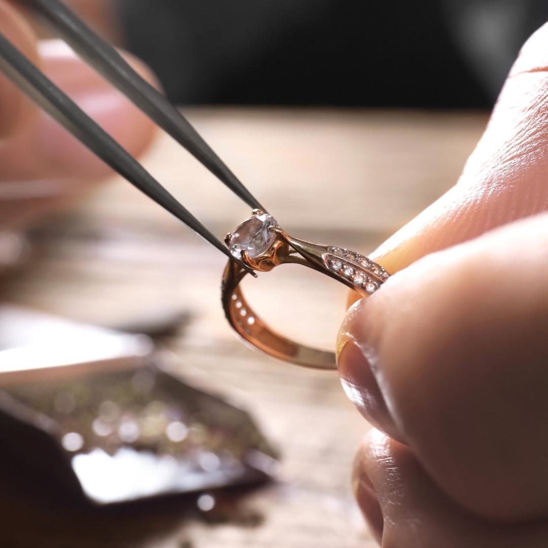 Eine Person hantiert mit einem Werkzeug an einem mit Edelstein besetzten Ring herum.