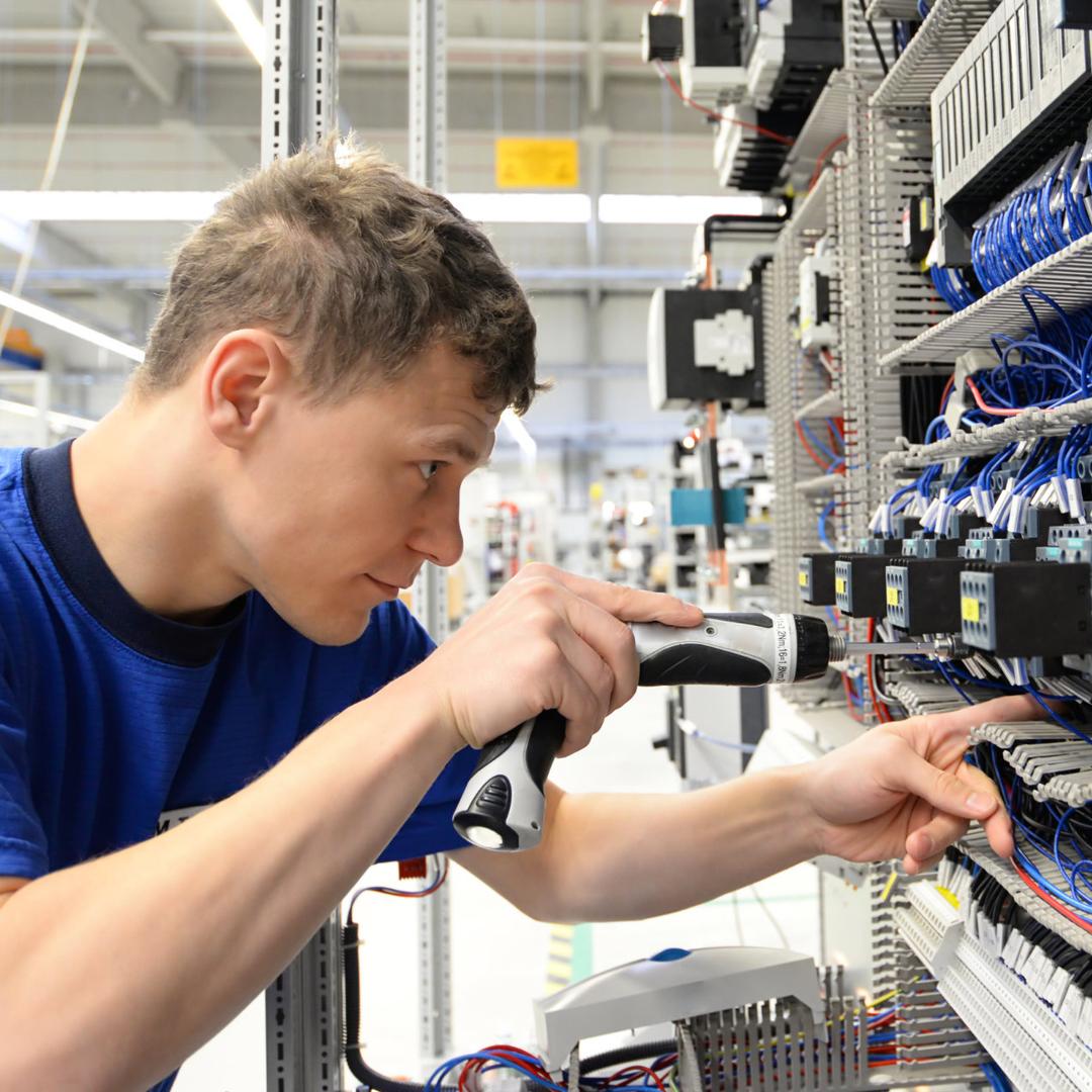 Ein junger Mann in Arbeitskleidung arbeitet konzentriert an einer elektrischen Anlage.