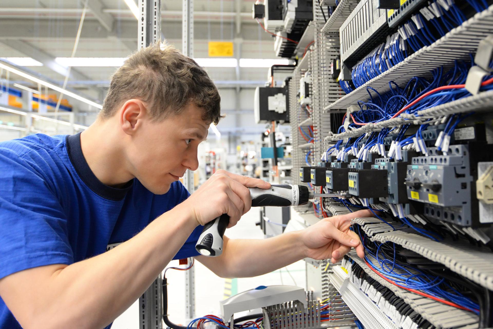 Ein junger Mann in Arbeitskleidung arbeitet konzentriert an einer elektrischen Anlage.