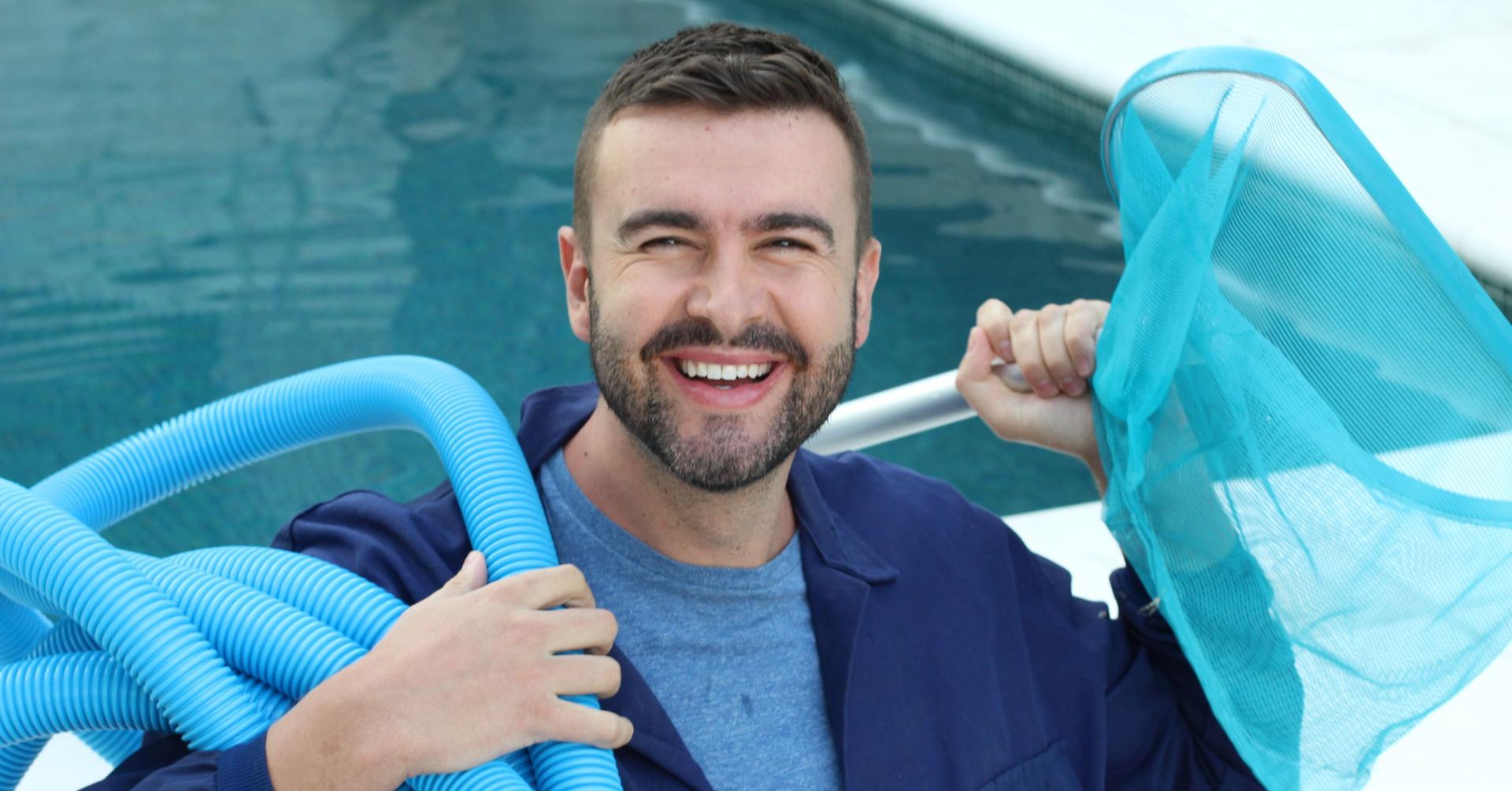 Ein Mann lächelt in die Kamera und hält neben einem Pool einen Schlauch und einen Kescher zur Reinigung in den Händen.