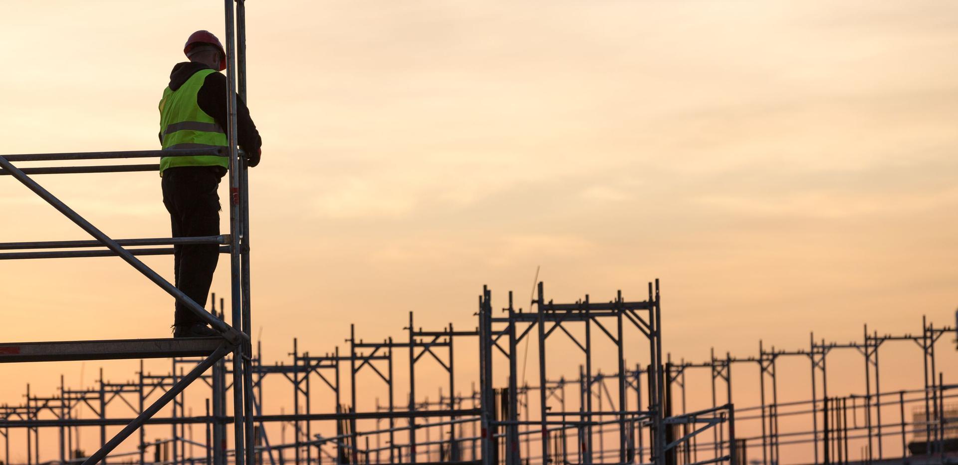 Ein Bauarbeiter steht auf einem Gerüst und arbeitet bei Sonnenuntergang auf einer Baustelle.