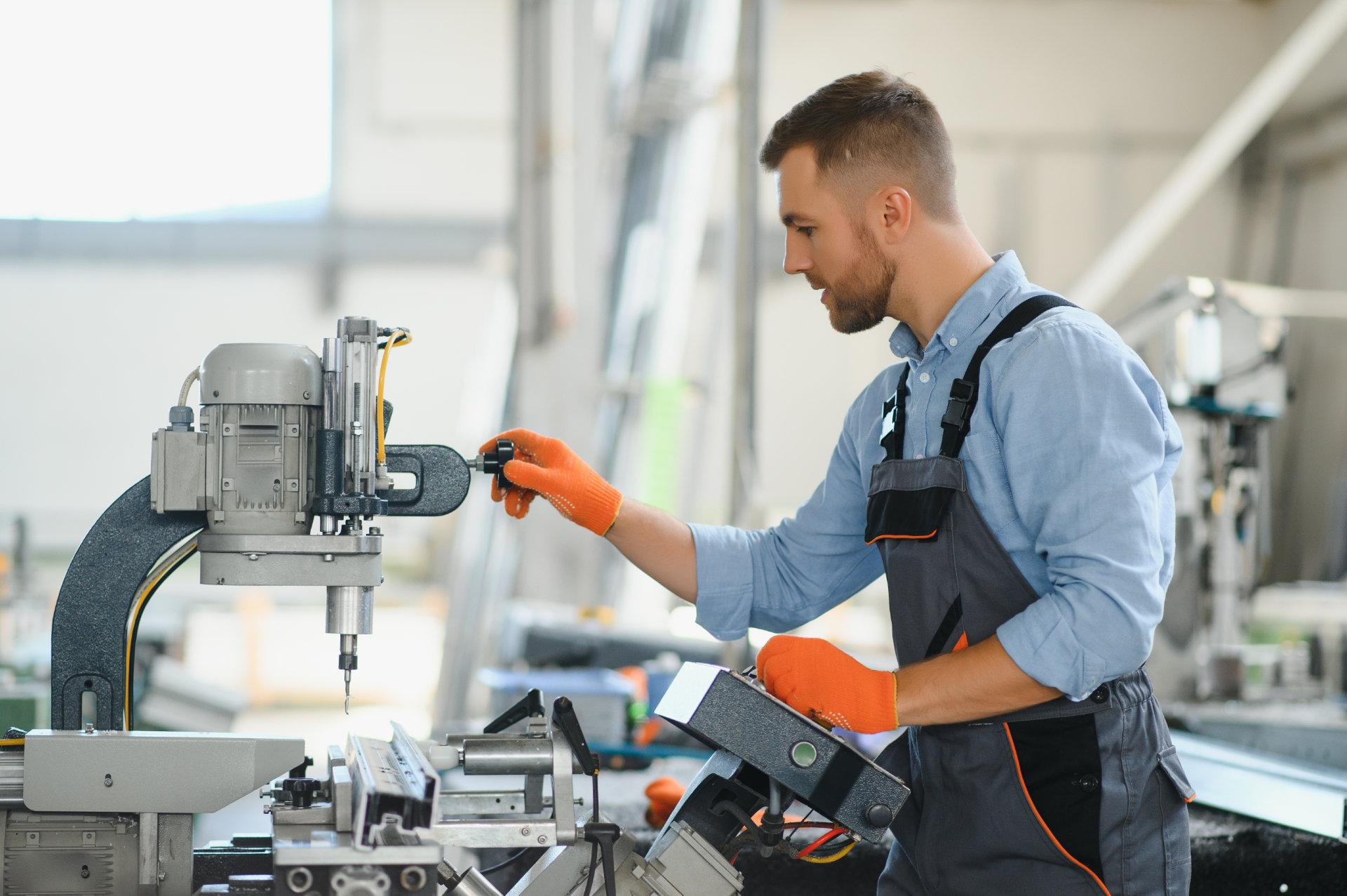 Ein Mann in Arbeitskleidung arbeitet an und mit einer industriellen Maschine.