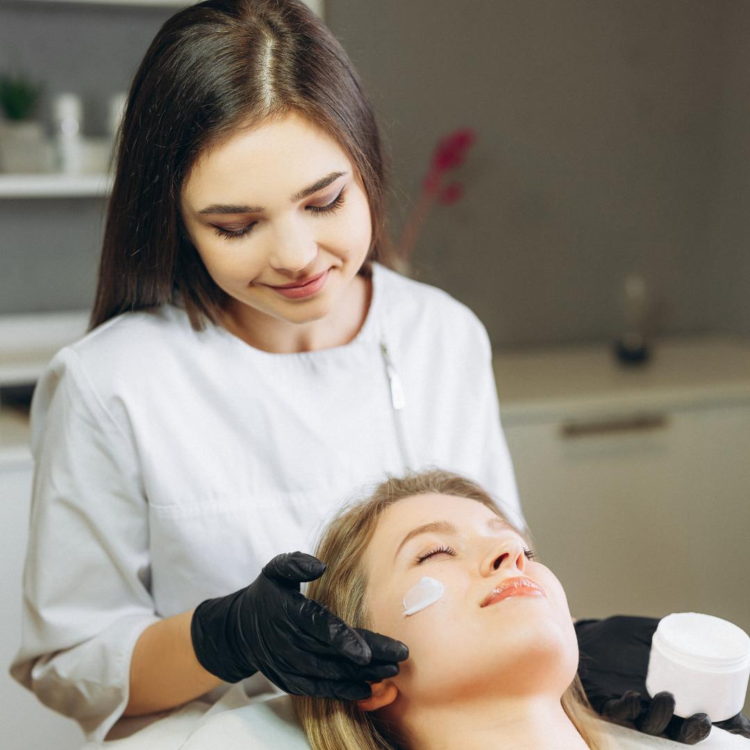 Eine Fachkraft führt eine kosmetische Behandlung durch und trägt ein Pflegeprodukt auf die Haut einer liegenden Person auf.
