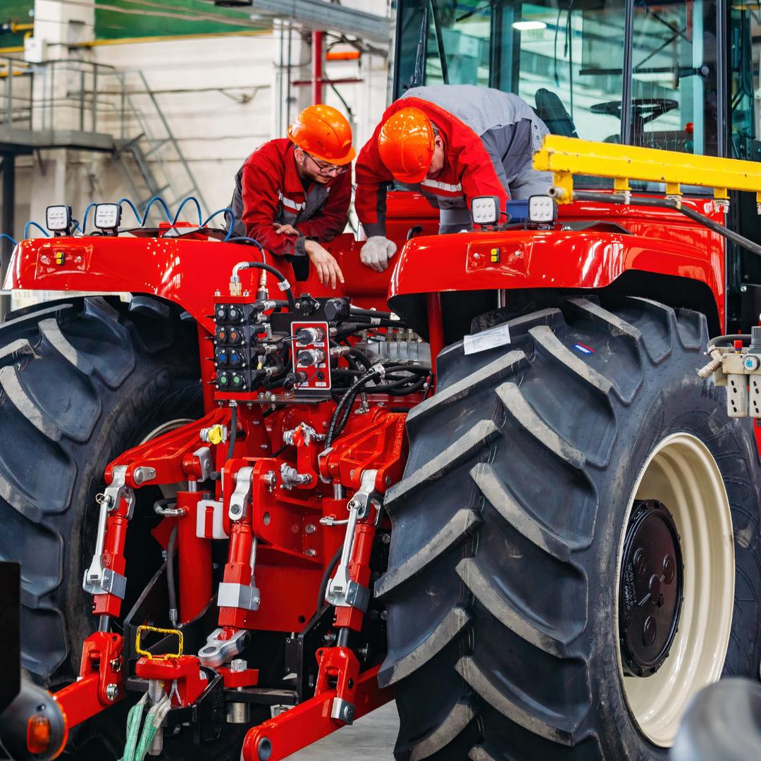 Zwei Land- und Baumaschinenmechatroniker in roter Arbeitskleidung stehen auf einer großen Landmaschine und schauen sich etwas an.