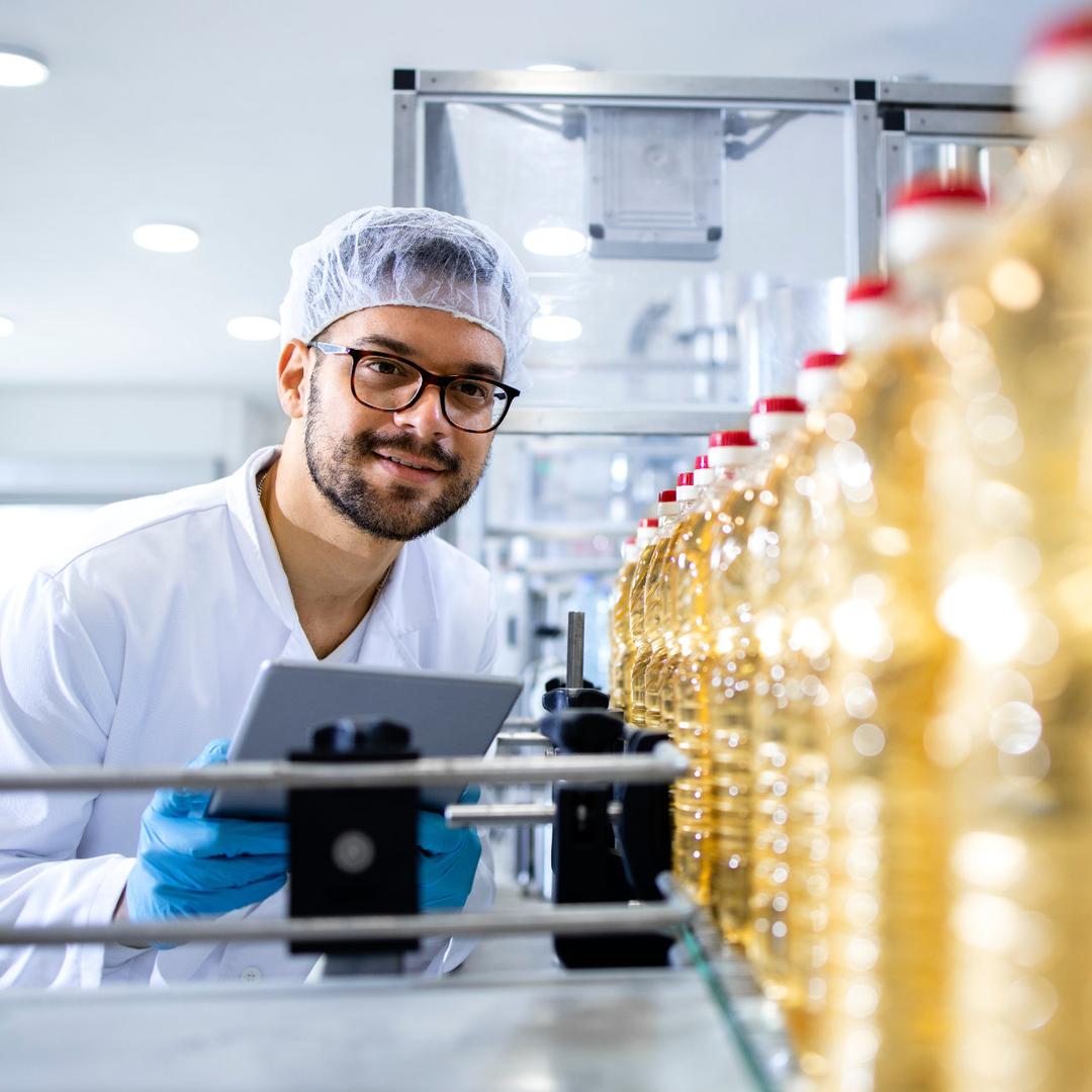 Ein Mann in Arbeitskleidung hält ein Tablet in der Hand während er Flaschen mit einer Lösung interessiert mustert.