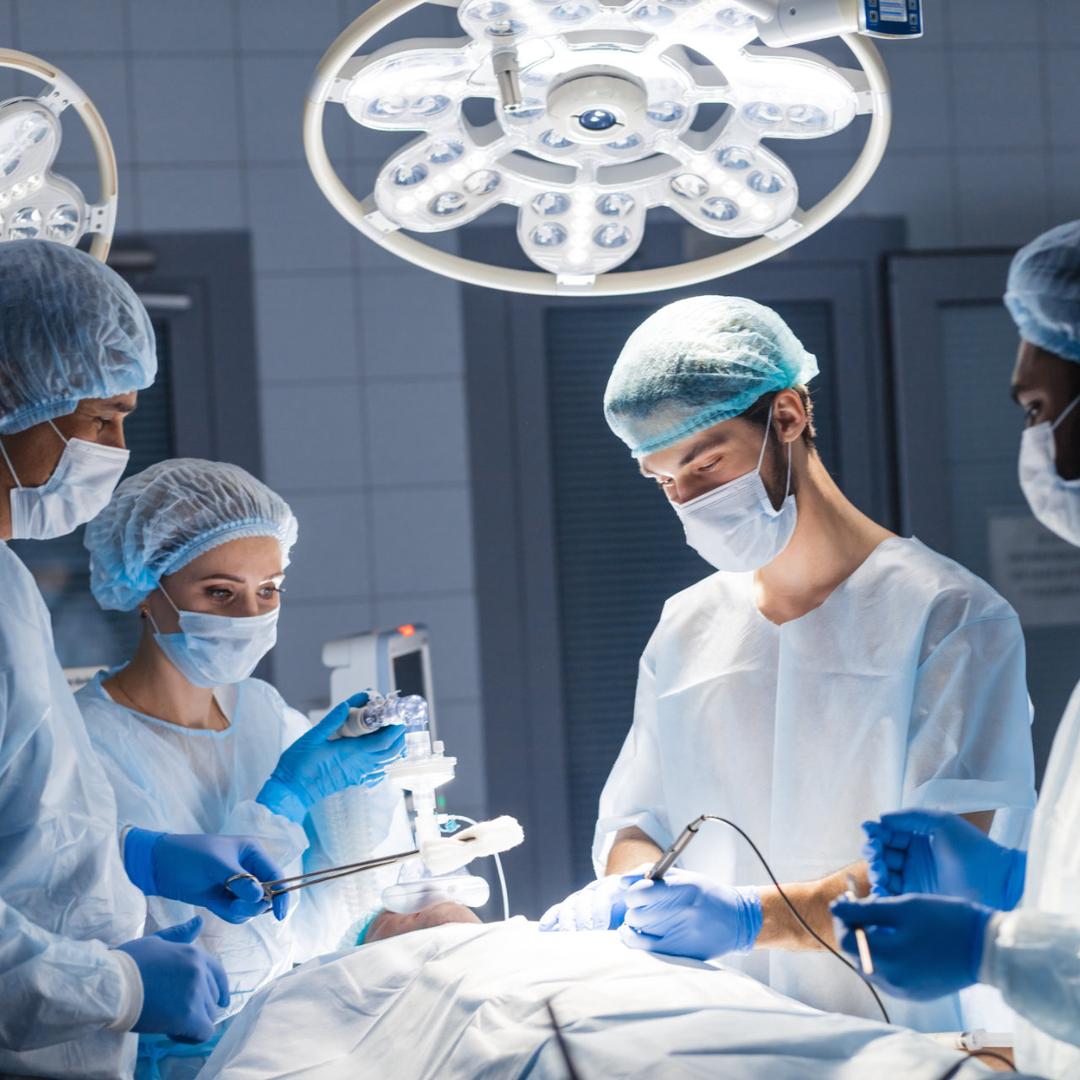 Ein Operationsteam in Schutzkleidung führt unter hellen OP-Lampen gemeinsam einen chirurgischen Eingriff durch.