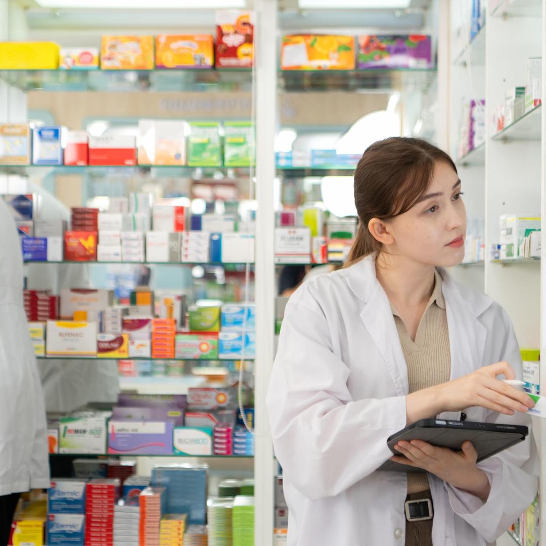 Zwei Personen in weißen Arbeitskitteln ordnen Medikamente in einer Apotheke ein und prüfen Bestände in den Regalen voller Arzneimittelverpackungen.