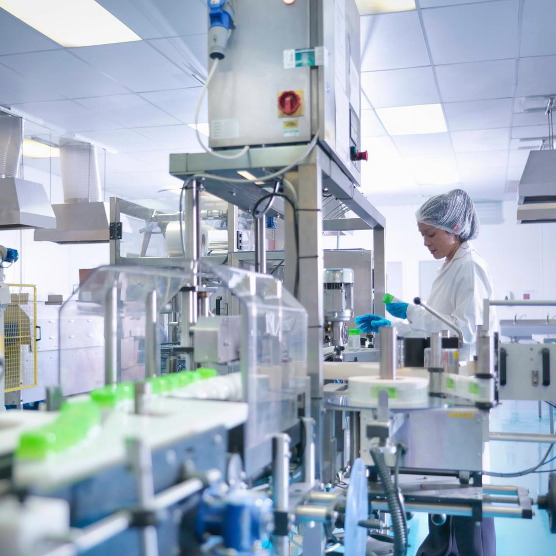 Eine Frau in Kittel arbeitet an einer Maschine.