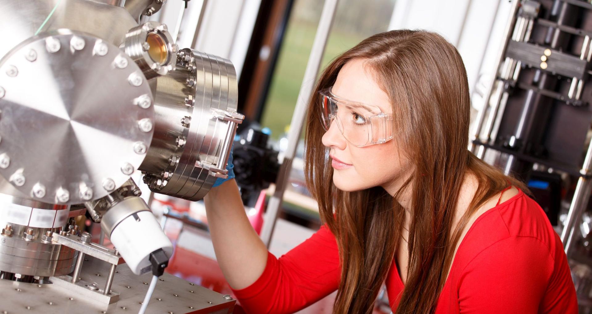 Eine Frau trägt eine Schutzbrille und schaut dabei konzentriert in eine Labormaschine.