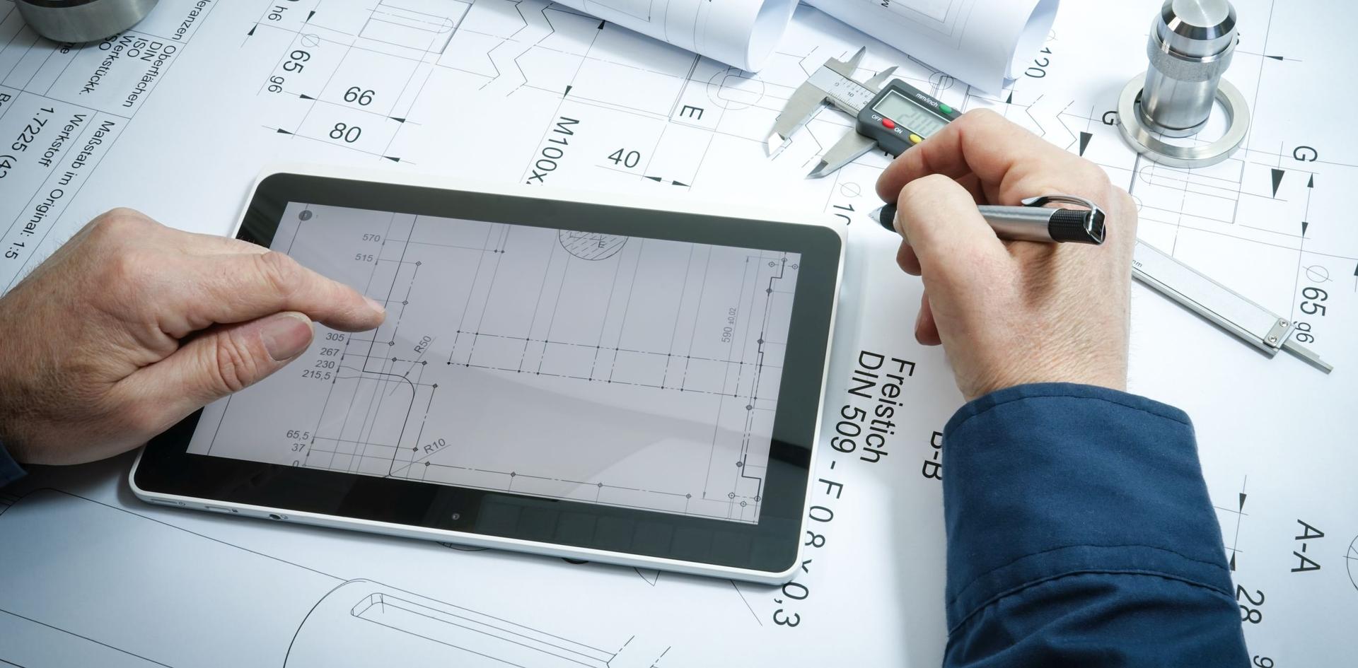 Ein Tablet auf dem Pläne zu sehen sind. Männliche Hände, die eine tippt auf das Tablet, die andere hält einen Stift. Im Hintergrund liegen ausgedruckte Pläne und Dokumente.